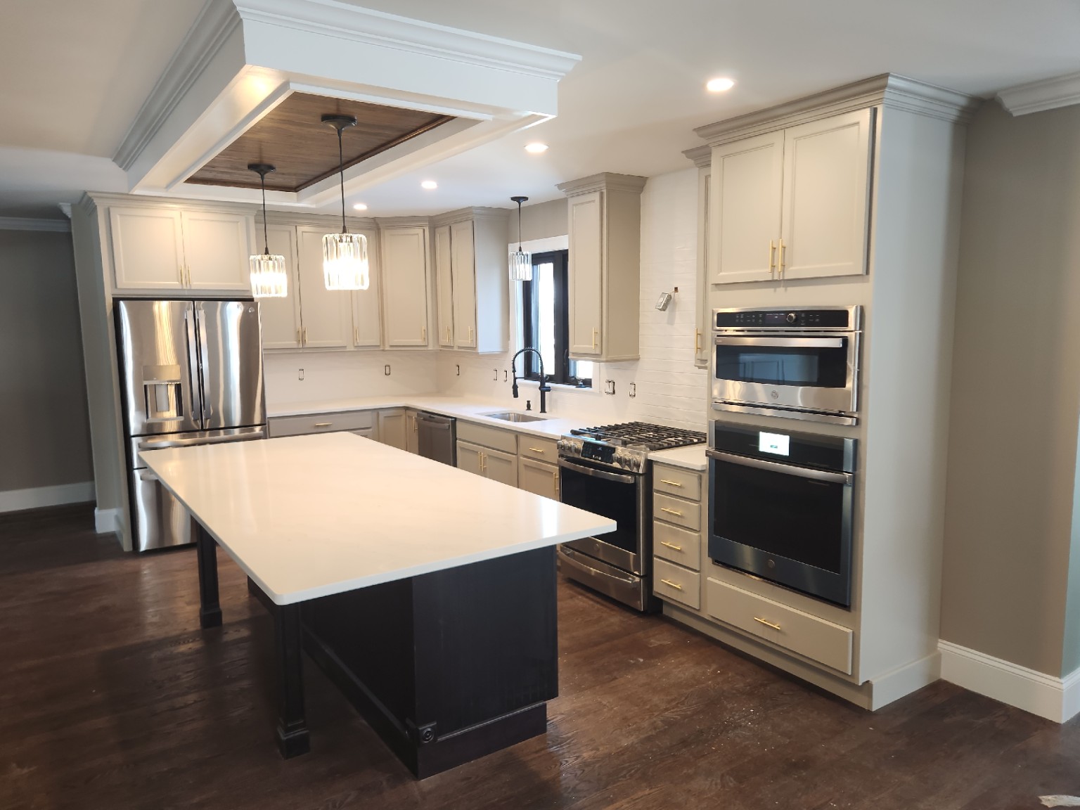 Cream kitchen cabinetry with crown molding, a dark island and a wood-inset ceiling feature